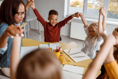 Smiling kids sitting at the table and raising their hands upの写真素材