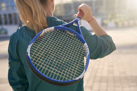 Close up shot of tennis racket in the hands of sportive woman, professional tennis player standing outdoors, ready for morning workoutの写真素材