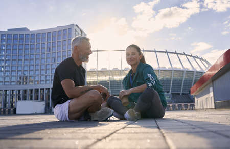 Sportive fit couple talking while sitting outdoors after morning workout on a sunny summer dayの写真素材