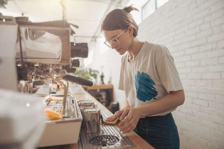 Charming female barista cleaning counter in coffee shopの写真素材