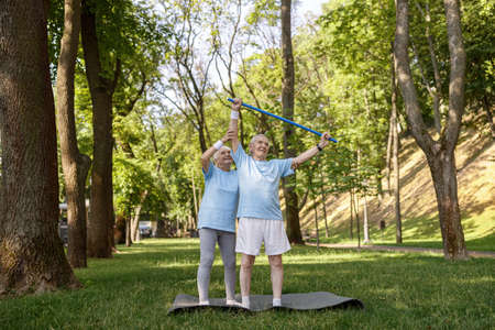 Careful senior woman helps husband to train with bar in green parkの写真素材