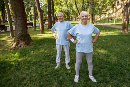 Cheerful senior woman and gentleman with hands on waist train in park on summer dayの写真素材