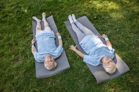 Relaxed senior man and woman lie on mats resting after training on fieldの写真素材