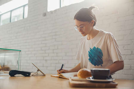 Charming female barista writing in notebook in coffee shopの写真素材