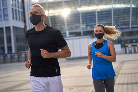 Active middle aged couple, man and woman wearing protective masks during morning run in urban environment. Covid19 responsible behaviorの写真素材