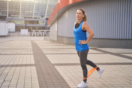 Motivated woman in sportswear stretching her legs using resistance band while training outdoors in the cityの写真素材