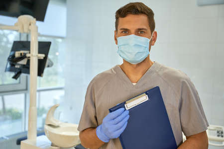 Attractive young dentist posing near dental chairの写真素材