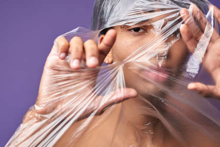 Close up horizontal portrait of young man tear up plastic bag with look eyes. Freedom of transgenderの写真素材