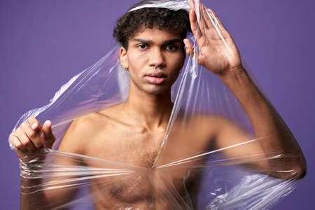 Young transgender man with destroy plastic bag on nude muscular body. Trans gender male can breatheの写真素材