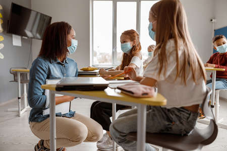 Young teacher talking to two schoolgirls in classの写真素材
