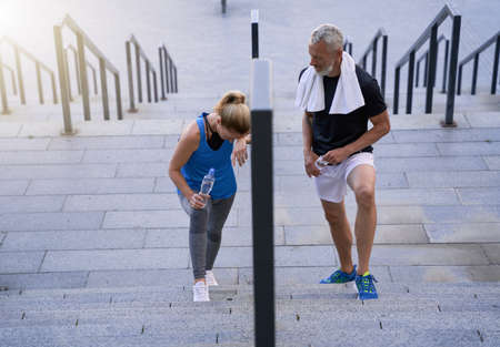 Tired middle aged couple, man and woman in sportswear walking up the stairs after exercising together outdoorsの写真素材