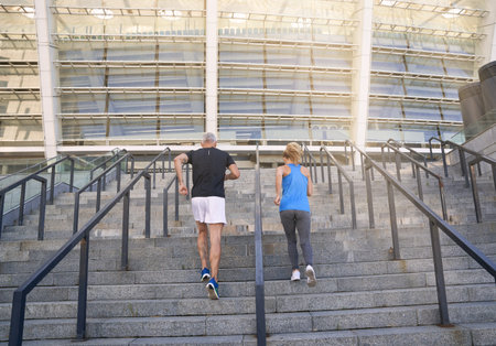 Back view of sporty couple in sportswear jogging while training together outdoors on the city stairsの写真素材