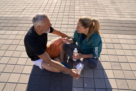 High angle view of mature couple in sportswear having a conversation while drinking water, relaxing outdoors on a sunny summer dayの写真素材