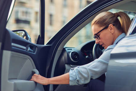 Coming to office. Caucasian middle aged business woman wearing eyeglasses getting out of her modern car, she is arrived at work in the morningの写真素材