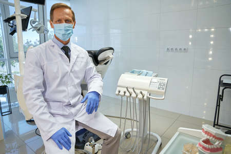 Proud dental specialist in uniform sitting at his officeの写真素材