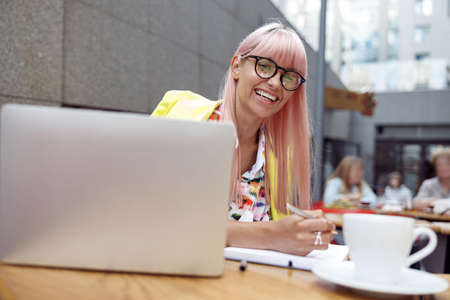 Optimistic woman in eyeglasses taking notes outdoors in cafeの写真素材