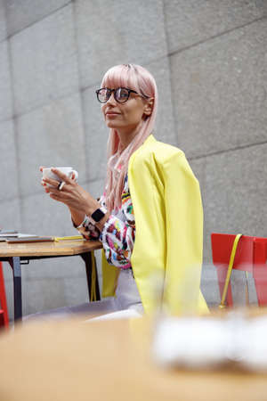 Fashionable woman in glasses drinking coffee outdoorsの写真素材