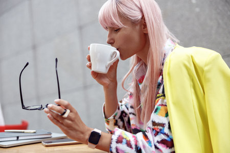 Hipster woman sipping coffee from cup at cafe table outdoorsの写真素材