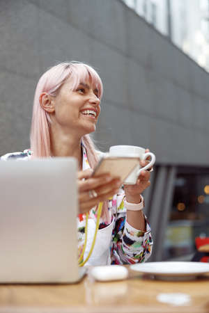 Joyful female smiling while drinking coffee in open airの写真素材