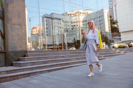 Cheerful woman with laptop walking on the streetの写真素材