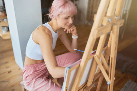 Happy artist draws picture with pencil sitting at wooden easelの写真素材