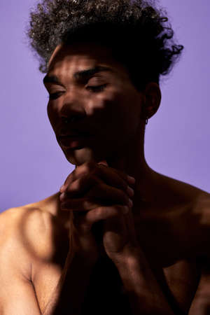 Portrait of african american man in shadow with pray pose. Transgender male stand with eyes closedの写真素材