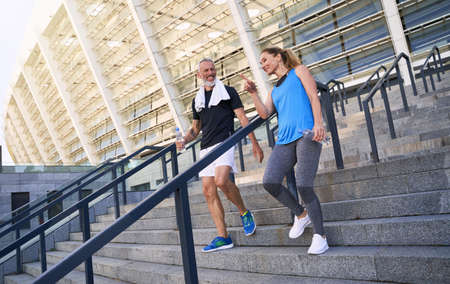 Sportive middle aged couple, man and woman in sportswear discussing something while walking down the stairs after training together outdoorsの写真素材