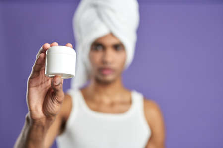 Attractive male show cream in hand bokeh portrait. Young african american man in white towel, t-shirtの写真素材