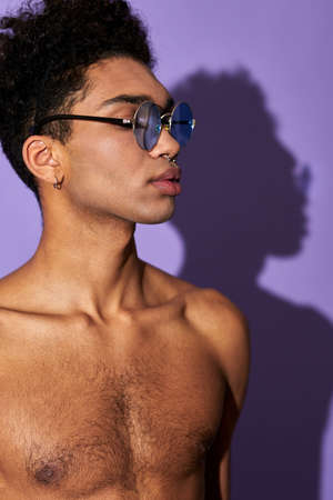 Close-up verticale portrait of young man in glasses with naked muscular torso on purple backgroundの写真素材