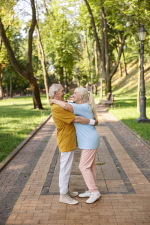 Cheerful senior couple in sportswear hugs standing on road in green parkの写真素材