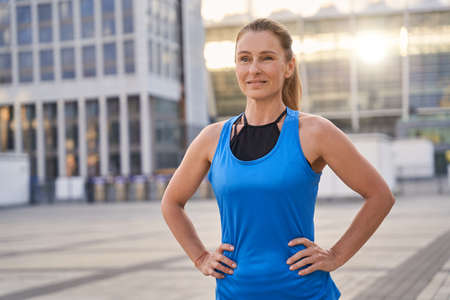 Portrait of attractive sportive middle aged woman in sportswear looking away, standing outdoors ready for running in the cityの写真素材