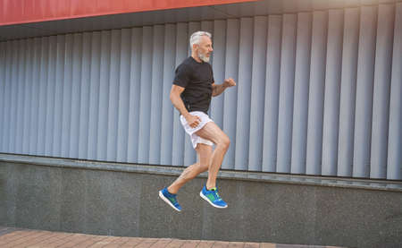 Active middle aged sportive man in sports clothing doing jump exercise while having workout outdoorsの写真素材
