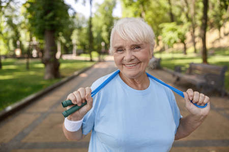 Pretty senior lady with jump rope poses for camera in green parkの写真素材
