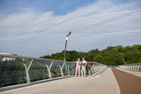 Positive sportive senior lady and man with rolled mats on footbridgeの写真素材