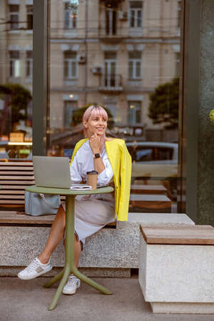 Cheerful young woman working on laptop at outdoor cafeの写真素材