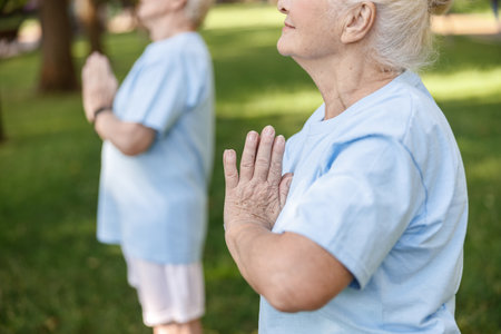Mature woman meditates with namaste mudra doing yoga with friend in green parkの写真素材