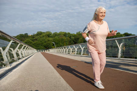 Smiling senior woman runs along empty footbridge in summer eveningの写真素材