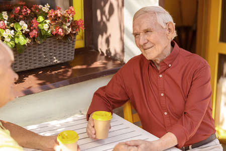 Cheerful senior gentleman spends time with beloved wife in street cafeの写真素材