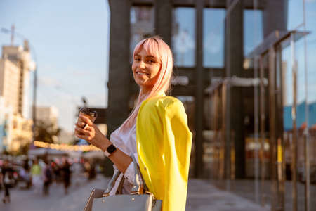 Joyful woman standing on the street and holding cup of coffeeの写真素材
