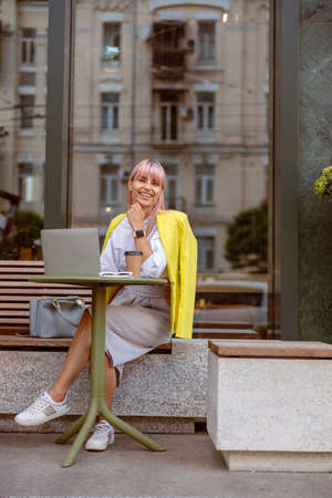 Cheerful woman sitting at the table with laptop on the streetの写真素材