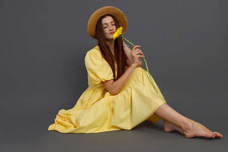 Charming woman in yellow dress smelling flower in studioの写真素材