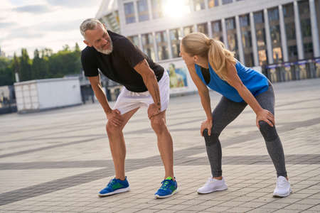 Mature couple, man and woman looking at each other, taking a short break while jogging together in the city on a warm summer dayの写真素材