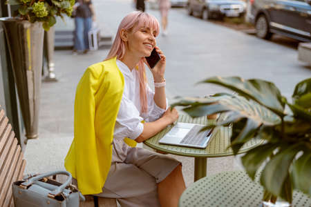 Cheerful woman having phone conversation at outdoor cafeの写真素材