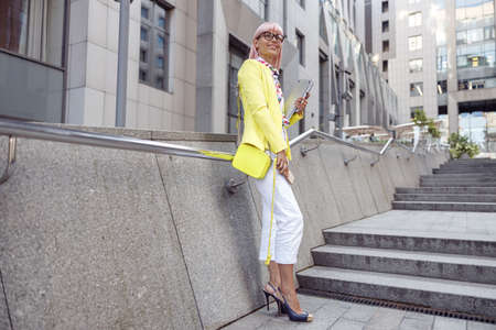 Brightly dressed lady carrying laptop while staying on stairsの写真素材