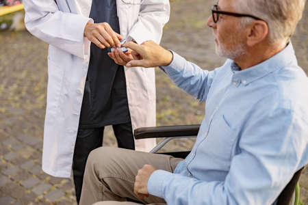 Doctor examining handicapped male patient in wheelchair with fingertip pulse oximeter outdoorsの写真素材