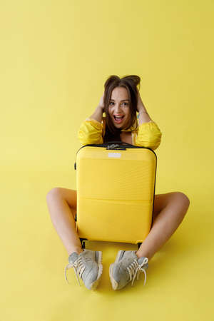 Joyful woman with trolley luggage bag posing in studioの写真素材
