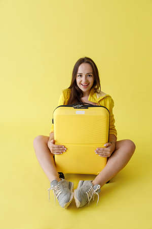 Joyful young woman with travel bag sitting in studioの写真素材