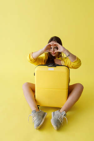 Charming young woman with travel suitcase doing heart signの写真素材