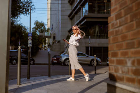 Cheerful woman standing on the street and listening to musicの写真素材