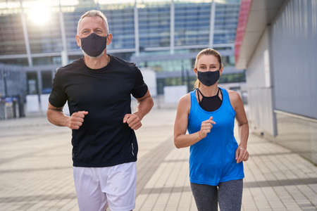 Sportive middle aged couple jogging with protective masks in the morning. Covid19 responsible behaviorの写真素材